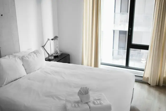 A freshly made bed with folded towels by a window